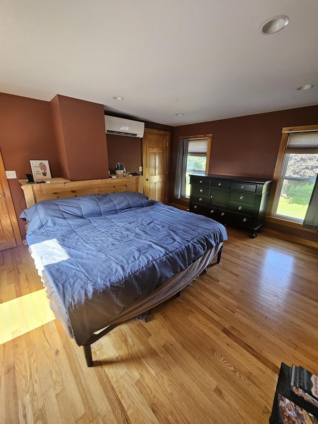 bedroom featuring multiple windows, a wall mounted air conditioner, and light hardwood / wood-style floors