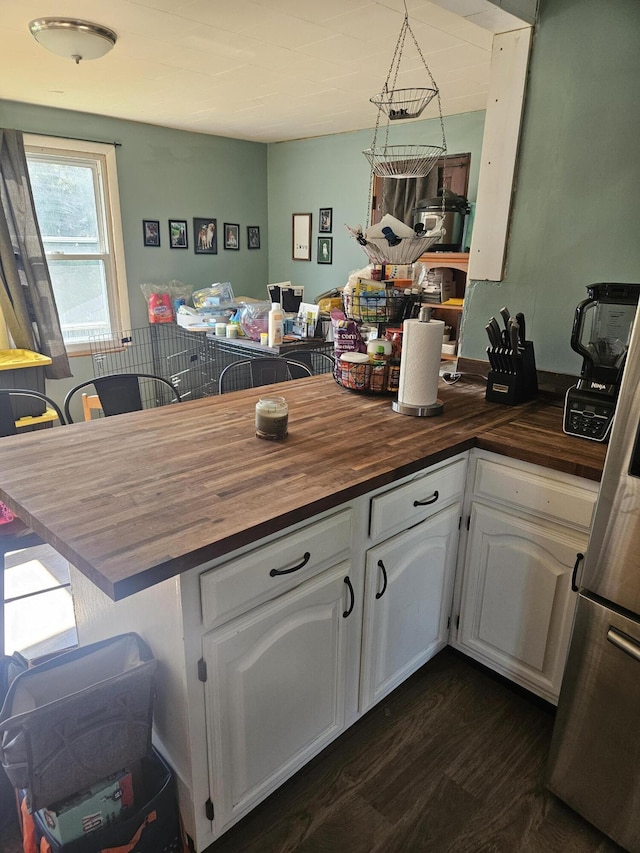 kitchen featuring white cabinetry, decorative light fixtures, stainless steel fridge, and wooden counters