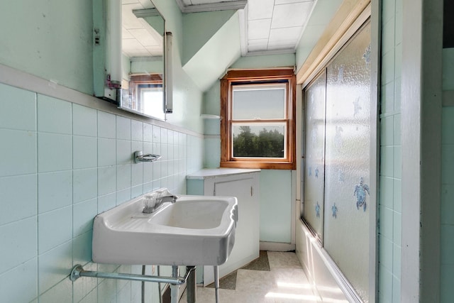 bathroom featuring sink, combined bath / shower with glass door, and tile walls