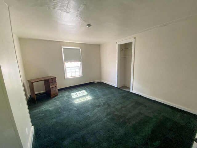 unfurnished bedroom featuring dark colored carpet, a closet, and baseboards