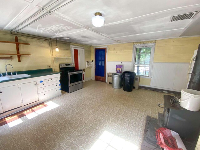 kitchen with light floors, stainless steel electric stove, visible vents, a sink, and wood walls