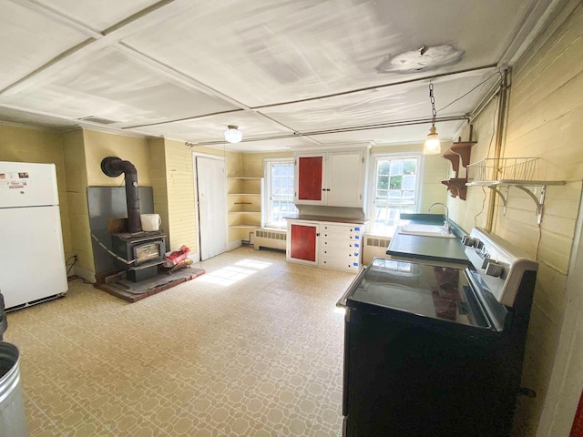 kitchen with a wood stove, radiator heating unit, freestanding refrigerator, and light floors