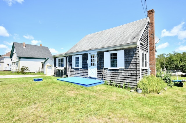 back of house featuring a chimney and a lawn