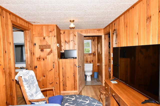 living area with light wood-style flooring, wooden walls, and crown molding