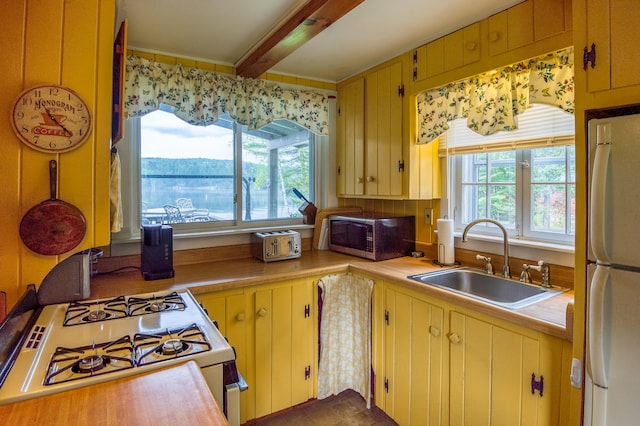 kitchen featuring stove, sink, white fridge, and beam ceiling