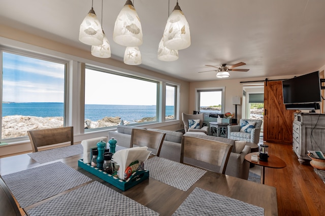 dining space featuring a water view, hardwood / wood-style floors, a barn door, and ceiling fan