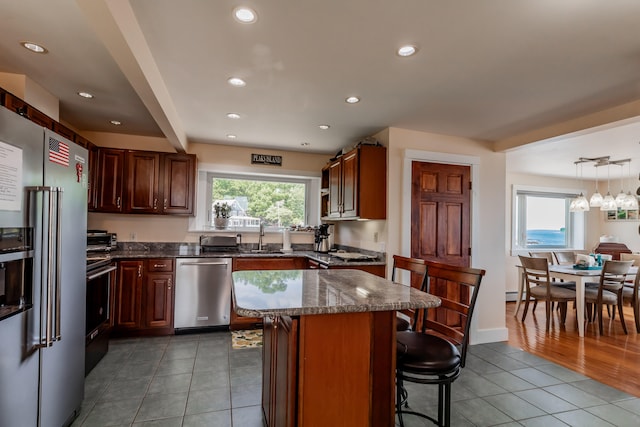 kitchen with a breakfast bar area, light hardwood / wood-style flooring, dark stone counters, hanging light fixtures, and appliances with stainless steel finishes