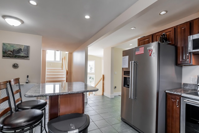 kitchen with light tile patterned flooring, stainless steel appliances, a kitchen bar, and stone countertops