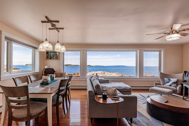 dining area featuring a water view, baseboard heating, light wood-type flooring, and ceiling fan