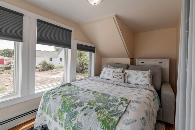 bedroom with a baseboard heating unit, hardwood / wood-style flooring, and vaulted ceiling