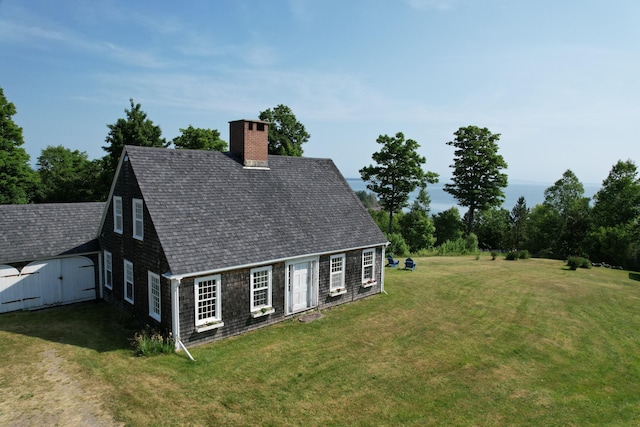 38 Kingsbury Ln, Perry, ME 04667 - view of home's exterior with a shingled roof, a chimney, a lawn, and a storage unit