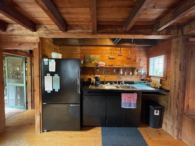 38 Kingsbury Ln, Perry, ME 04667 - kitchen with freestanding refrigerator, wooden walls, a wood ceiling with exposed beams, dark countertops, and light wood finished floors