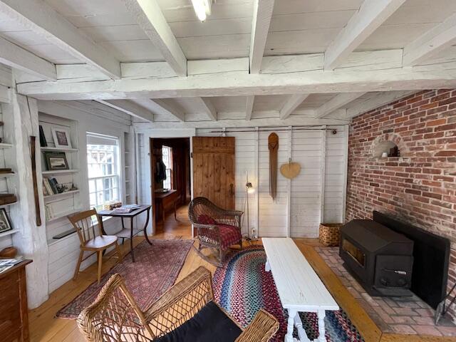 38 Kingsbury Ln, Perry, ME 04667 - living area featuring a wood stove, beamed ceiling, wood-type flooring, wooden walls, and brick wall