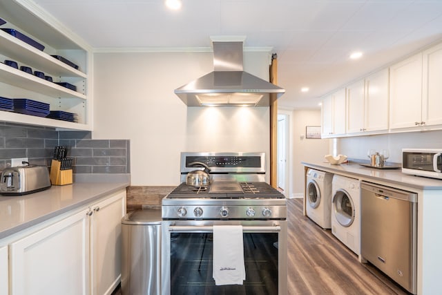 kitchen with wall chimney range hood, decorative backsplash, hardwood / wood-style floors, appliances with stainless steel finishes, and washing machine and clothes dryer