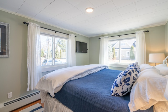 bedroom with multiple windows, ornamental molding, baseboard heating, and hardwood / wood-style floors