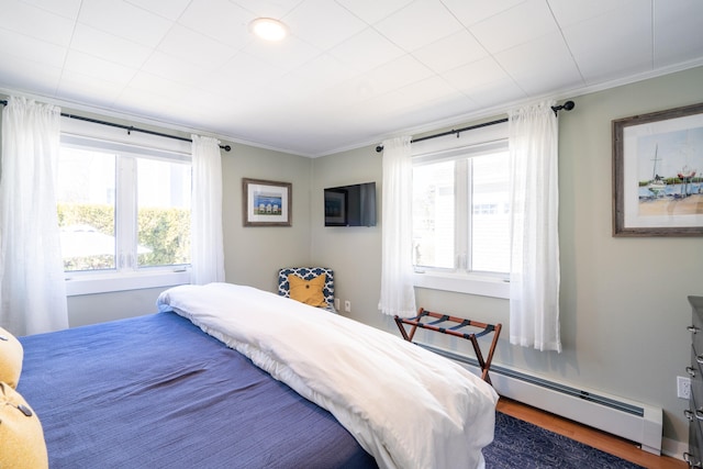 bedroom with ornamental molding, a baseboard heating unit, and hardwood / wood-style floors