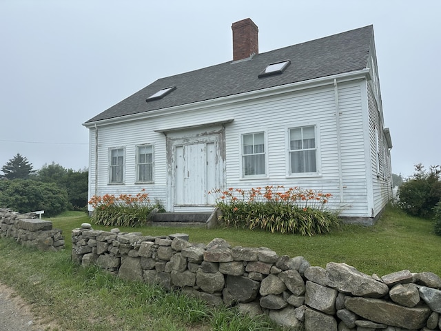 view of front of house featuring roof with shingles, a chimney, and a front lawn