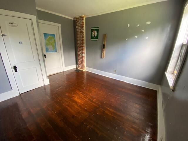 empty room with brick wall, ornamental molding, and wood-type flooring