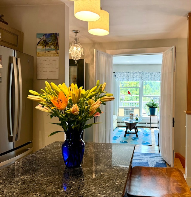 kitchen featuring dark stone counters, wood-type flooring, pendant lighting, an inviting chandelier, and stainless steel refrigerator