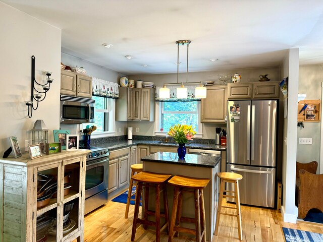 kitchen featuring a kitchen bar, stainless steel appliances, light hardwood / wood-style floors, decorative light fixtures, and a kitchen island