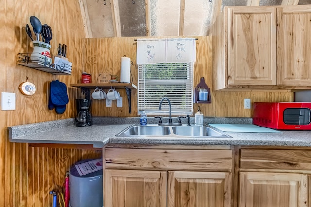 kitchen featuring light brown cabinetry, sink, and wooden walls