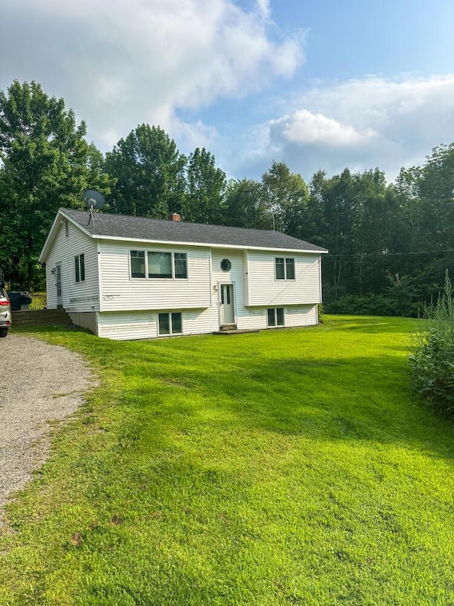 split foyer home with entry steps, gravel driveway, a chimney, and a front lawn