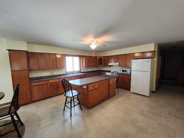 kitchen with ceiling fan, light tile patterned floors, white fridge, and a kitchen island