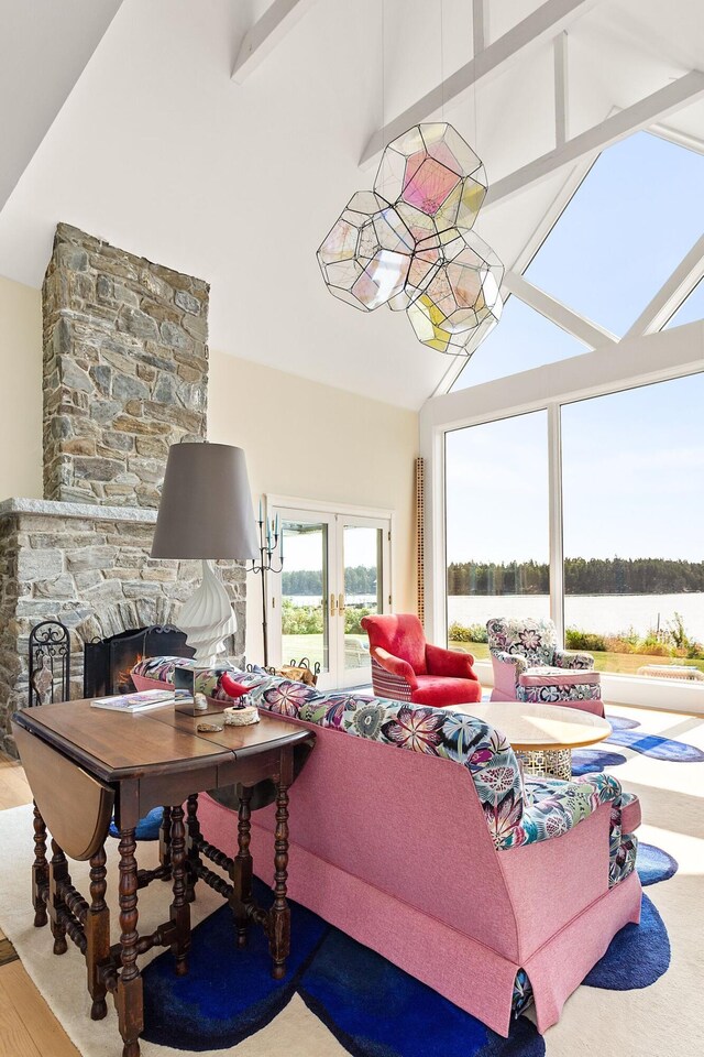 living room with wood-type flooring, a water view, beamed ceiling, french doors, and a stone fireplace