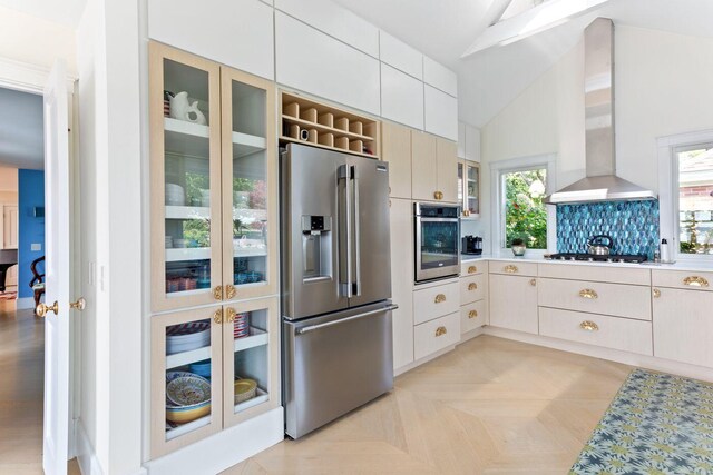 kitchen featuring light parquet flooring, decorative backsplash, high vaulted ceiling, wall chimney exhaust hood, and appliances with stainless steel finishes