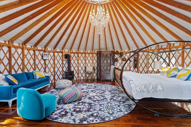 bedroom with an inviting chandelier, hardwood / wood-style flooring, vaulted ceiling, and a wood stove