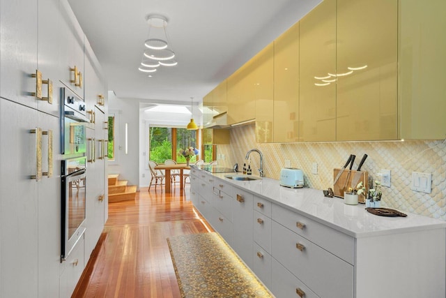 kitchen featuring sink, stainless steel oven, decorative light fixtures, and light wood-type flooring