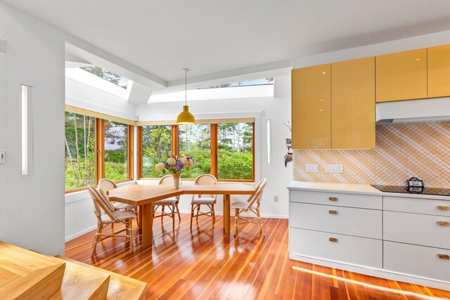 dining room with vaulted ceiling with skylight and light wood-type flooring