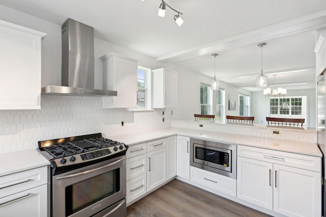 kitchen with appliances with stainless steel finishes, tasteful backsplash, hardwood / wood-style floors, wall chimney range hood, and hanging light fixtures