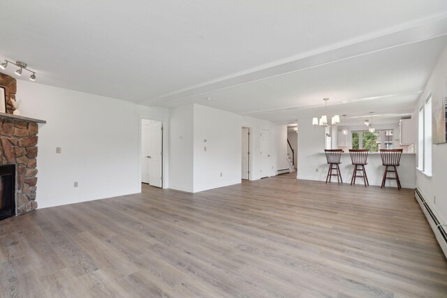 unfurnished living room featuring track lighting, hardwood / wood-style floors, a stone fireplace, a baseboard heating unit, and a notable chandelier