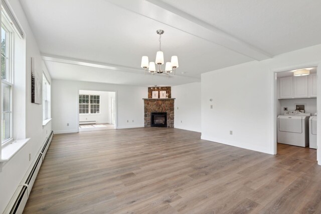 unfurnished living room with baseboard heating, wood-type flooring, a stone fireplace, and washing machine and clothes dryer