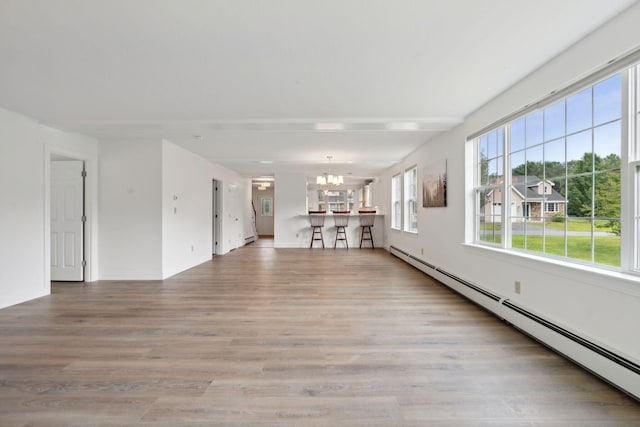 unfurnished living room featuring wood-type flooring, a baseboard radiator, and a chandelier