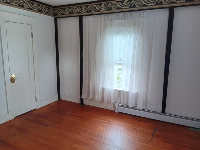 spare room with wood-type flooring and a baseboard heating unit