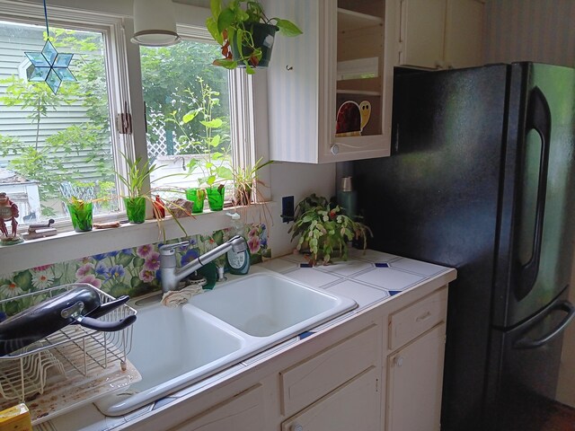 kitchen with white cabinetry, black refrigerator, hanging light fixtures, and sink