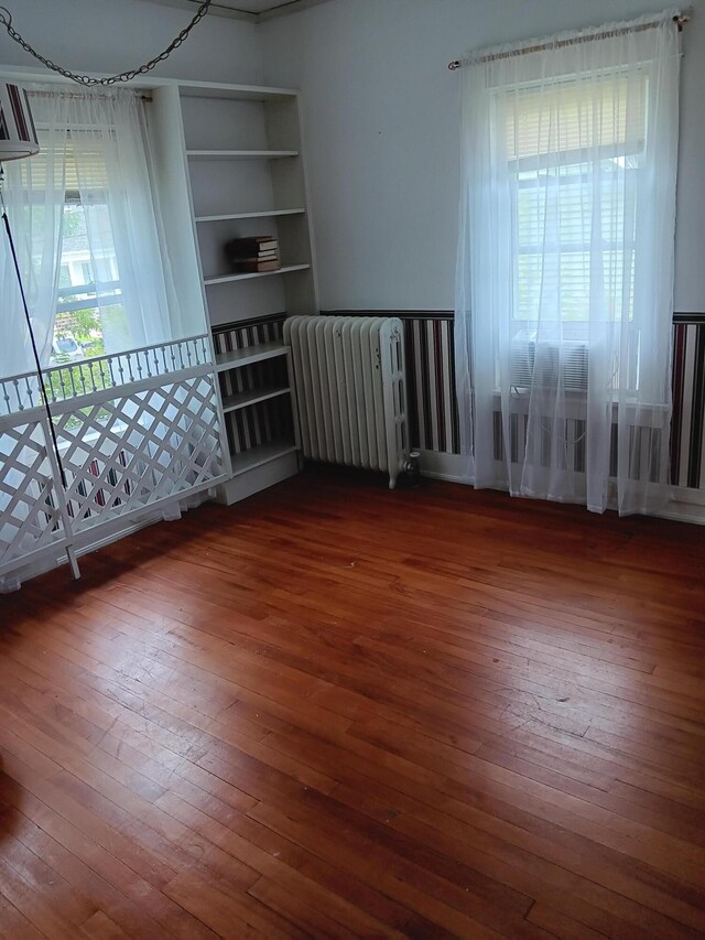 empty room with built in features, radiator, and hardwood / wood-style floors