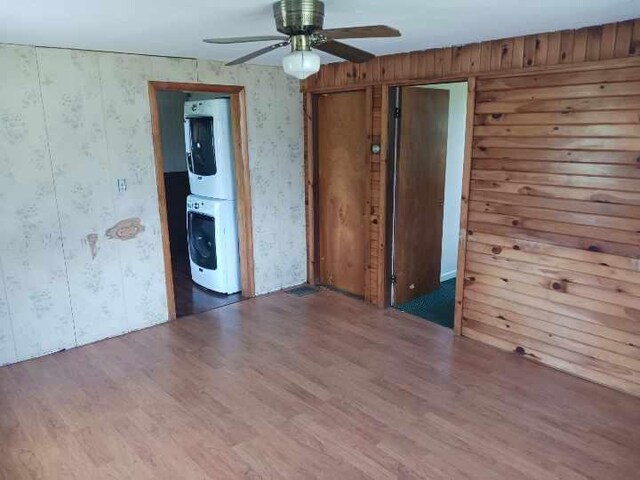 empty room with hardwood / wood-style floors, stacked washer / drying machine, wooden walls, and ceiling fan