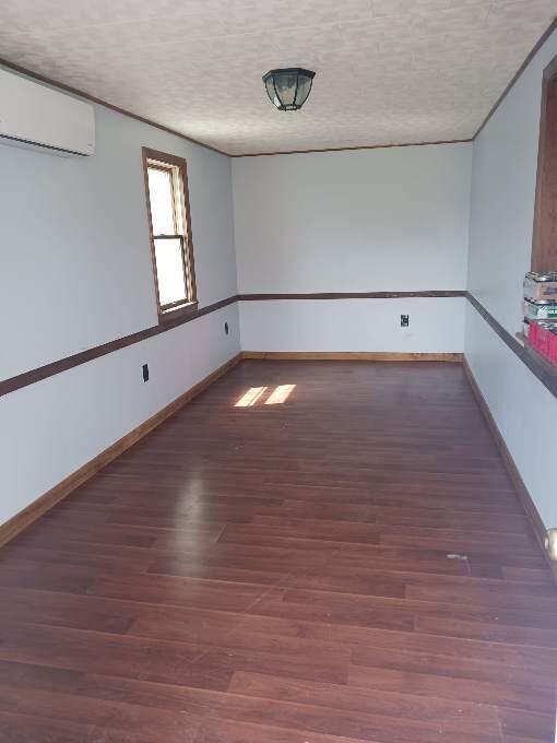 empty room featuring an AC wall unit, hardwood / wood-style floors, and a textured ceiling