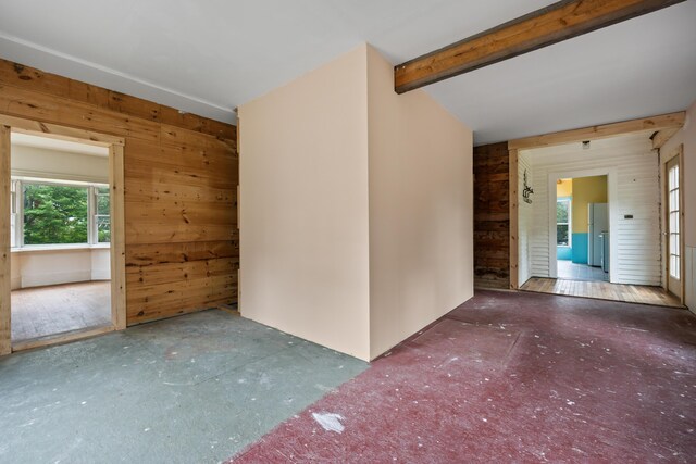 spare room featuring wooden walls, beamed ceiling, and wood-type flooring