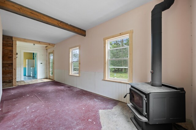 interior space with wood walls, beam ceiling, and a wood stove