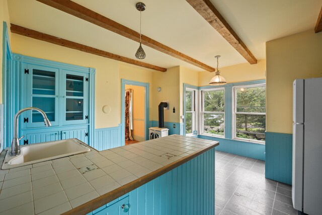 kitchen featuring beam ceiling, a wood stove, tile counters, hanging light fixtures, and white refrigerator