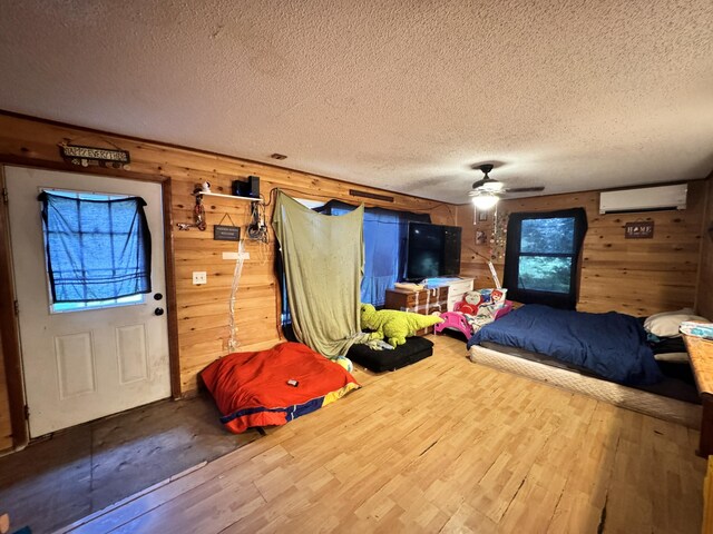 game room with ceiling fan, a wall mounted air conditioner, wood walls, hardwood / wood-style floors, and a textured ceiling