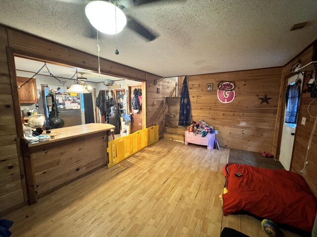 interior space featuring a textured ceiling, light hardwood / wood-style floors, ceiling fan, and wooden walls