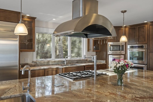 kitchen featuring stone counters, island range hood, sink, hanging light fixtures, and built in appliances