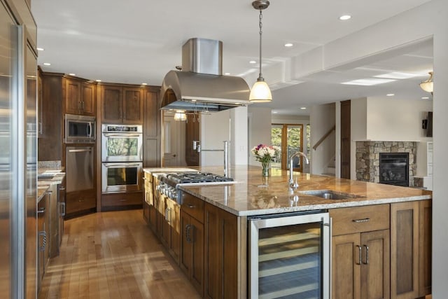 kitchen with wine cooler, sink, island range hood, built in appliances, and a large island with sink