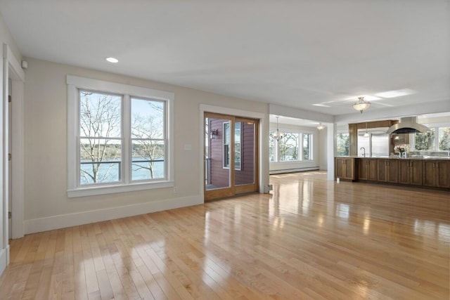 unfurnished living room with a baseboard radiator, sink, a chandelier, and light hardwood / wood-style floors