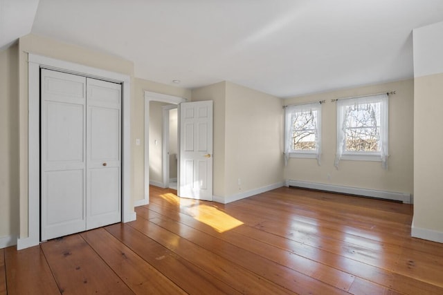 unfurnished bedroom with hardwood / wood-style floors, baseboard heating, and a closet